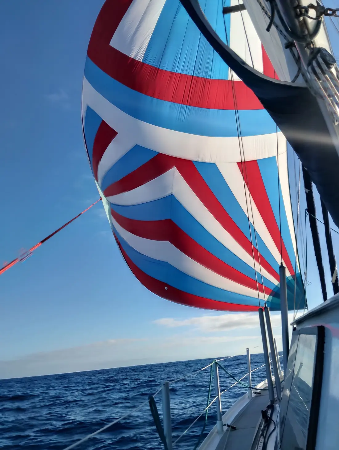 Blue, white and red spinnaker filled with wind above the ocean